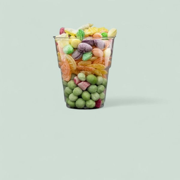 Verre rempli de bonbons assortis aux couleurs vives — verts, jaunes, oranges, violets et roses — mélange de dragées, berlingots et confiseries fruitées.