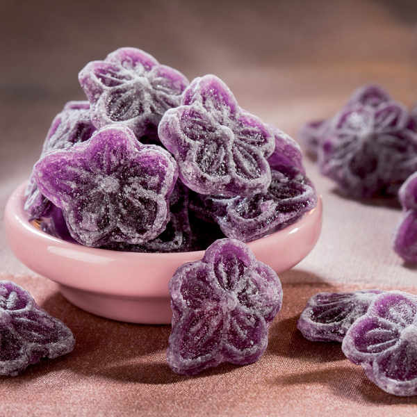 Bonbons à la violette dans une coupelle rose sur fond en tissu, confiseries colorées au parfum de violette de Toulouse.