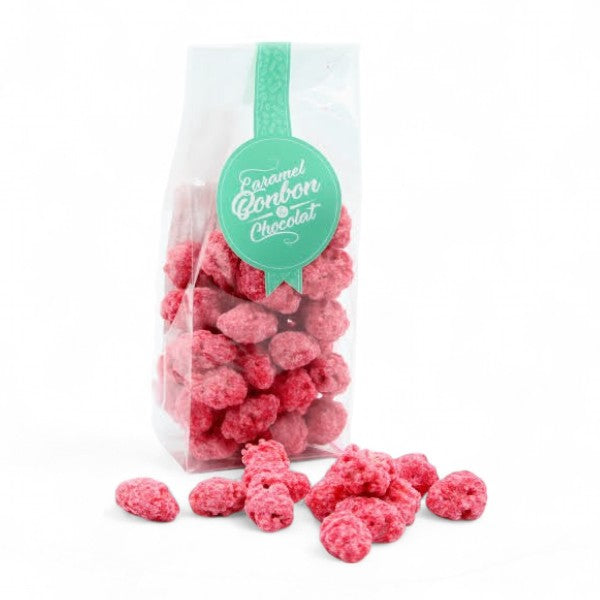 Sachet de pralines rouges entières aux amandes sur fond blanc, confiserie croquante au sucre cuit et amandes torréfiées.