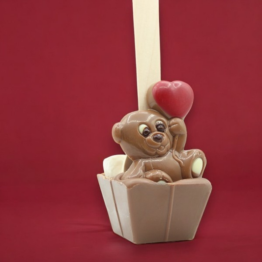 Cuillère à chocolat chaud Ourson Cœur présentée sur fond rouge, chocolat au lait fondant en forme d’ourson pour une pause gourmande et réconfortante.