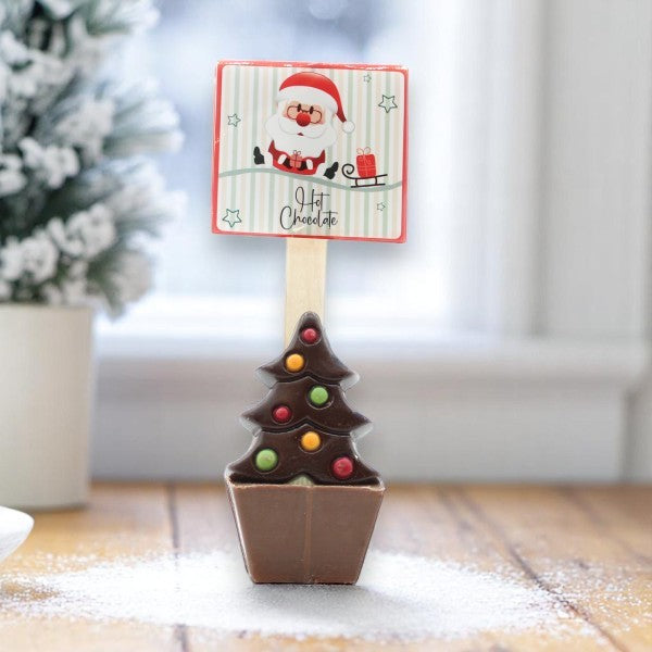 Cuillère à chocolat chaud de Noël présentée dans une ambiance festive, chocolat décoré d’un sapin et garni de mini guimauves pour une boisson gourmande et réconfortante.