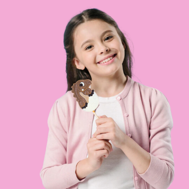 Fillette tenant une sucette dinosaure en chocolat au lait, moment joyeux et gourmand plein de fantaisie.