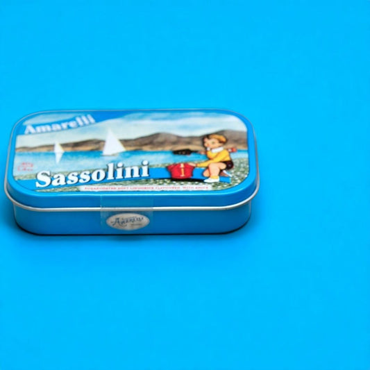 Boîte métallique de réglisses Sassolini sur fond bleu, confiserie italienne à la réglisse et à l’anis, au design élégant.