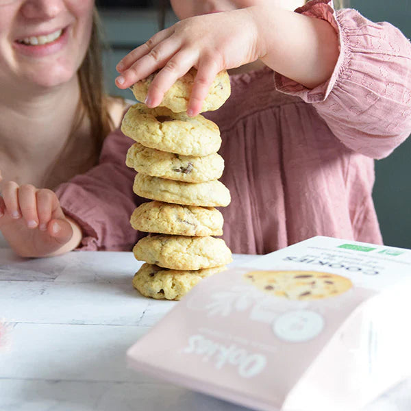 Enfant faisant une pile de cookies au chocolat au lait et noisettes, scène joyeuse et gourmande autour de biscuits faits maison.