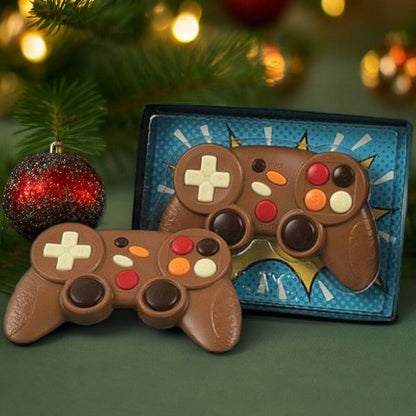 Manette de jeux vidéo en chocolat au lait placée sous un sapin de Noël, cadeau sucré et amusant pour fêtes de fin d’année.