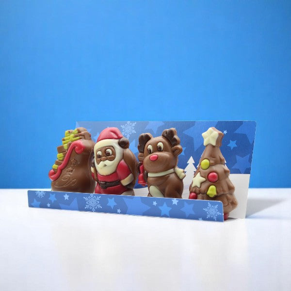 Coffret de moulages en chocolat Figurines de Noël 120g sur fond bleu, chocolats au lait et blanc festifs et gourmands.