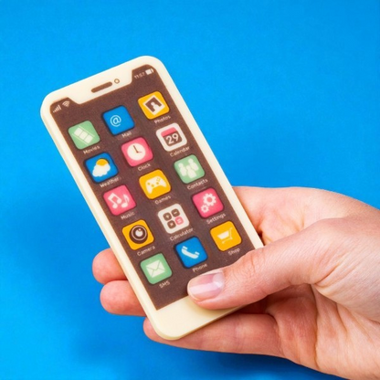 Smartphone en chocolat au lait tenu dans une main sur fond bleu, gourmandise réaliste et cadeau original pour amateurs de chocolat.