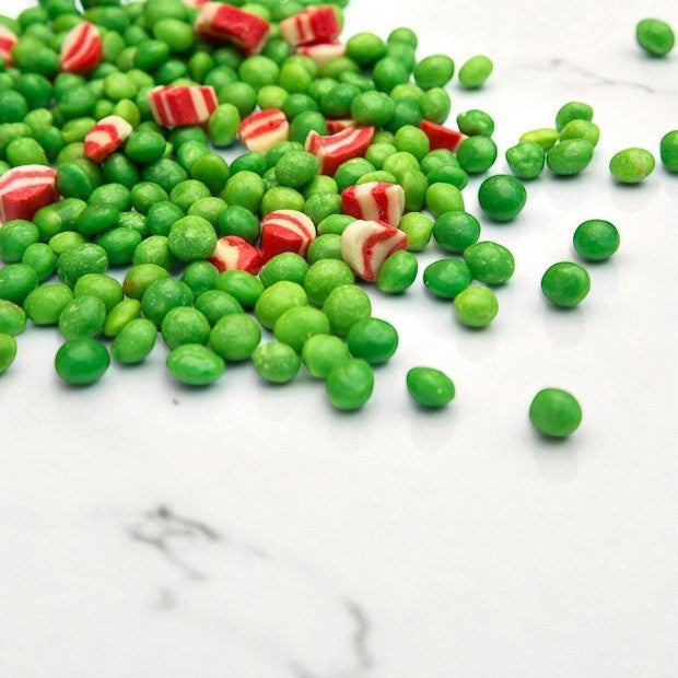 Bonbons Pois au lard en vrac, confiseries dragéifiées vertes à l’anis ornées de morceaux roses et blancs rappelant des lardons.