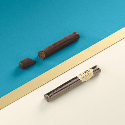 Cigare italien en chocolat noir à l’écorce d’orange présenté sur fond bleu, création élégante et raffinée au goût intense.
