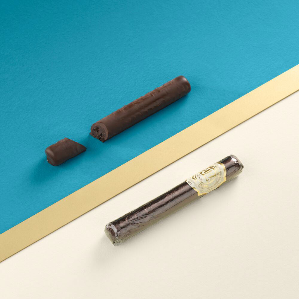 Cigare italien en chocolat noir présenté sur fond bleu, confiserie raffinée à la pâte de noisettes et au cacao aromatique.