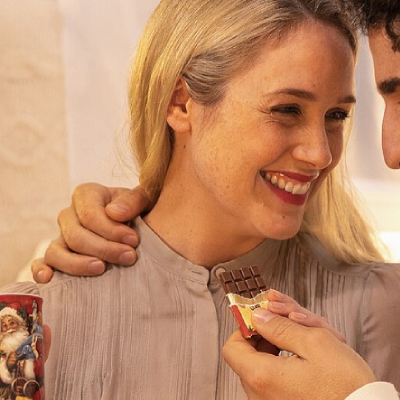 Femme ouvrant une mini tablette “Nostalgie” de Noël en chocolat au lait, moment gourmand et chaleureux aux saveurs festives.