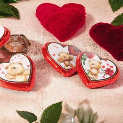 Quatre Cœurs Ourson en chocolat au lait disposés sur une nappe en décoration, gourmandises pralinées aux motifs colorés et joyeux.