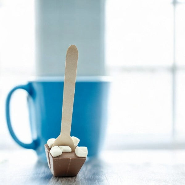 Cuillère à chocolat chaud au lait et mini guimauves dans une tasse bleue – boisson gourmande et onctueuse pour moment cocooning.