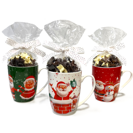 Trois mugs de Noël en céramique décorée, garnis de chocolats au lait en forme d’étoile, aux couleurs vert, rouge et blanc.