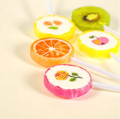 Cinq sucettes Rock “Fleurs et Fruits” posées sur une table – confiseries colorées aux goûts fruités variés.