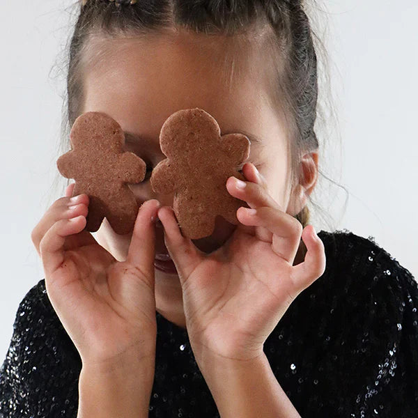Petite fille cachant ses yeux avec deux biscuits pain d’épices, scène joyeuse et gourmande autour des biscuits faits maison.