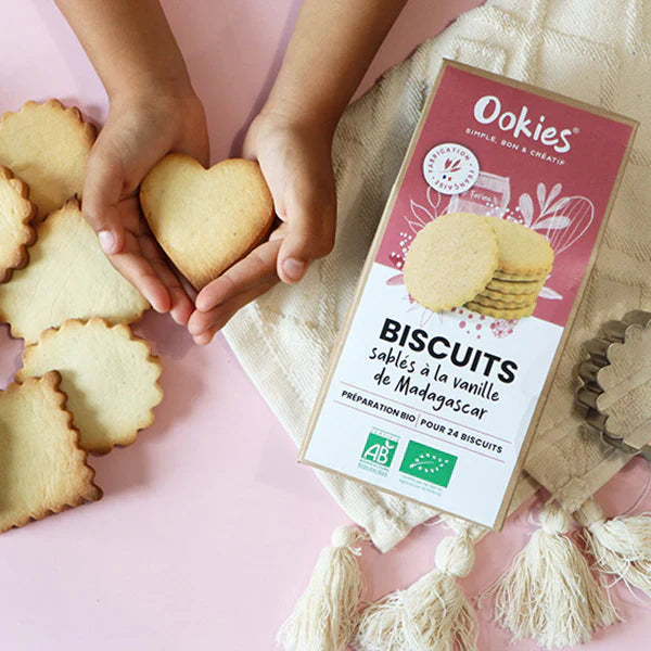 Petites mains tenant un biscuit sablé à la vanille de Madagascar, gourmandise dorée et fondante préparée avec la préparation bio.