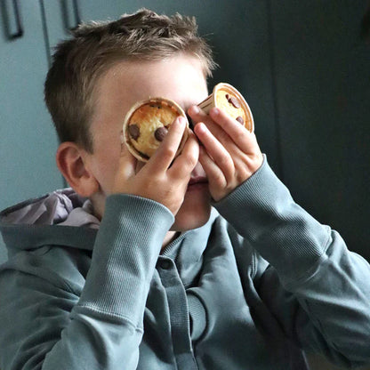 Garçon cachant ses yeux avec deux muffins aux pépites de chocolat, scène amusante et gourmande autour des muffins bio faits maison.