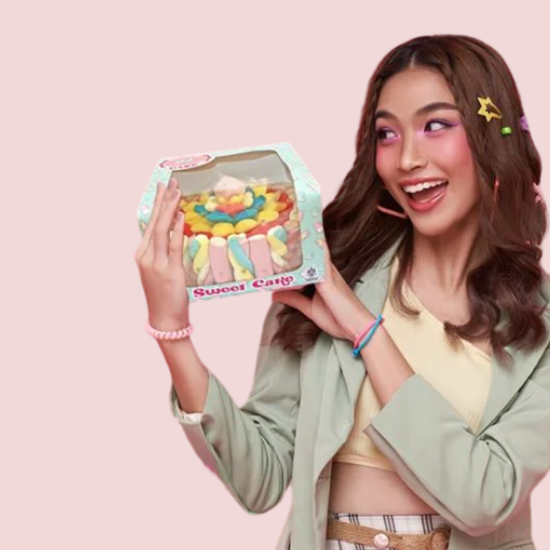 Fille tenant un gâteau de bonbons en étages rond “Sweet Cake” – pièce sucrée décorée de guimauves et friandises festives.