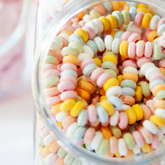 Boîte de 100 colliers de bonbons en dextrose, anneaux colorés pastel enfilés sur un fil élastique.