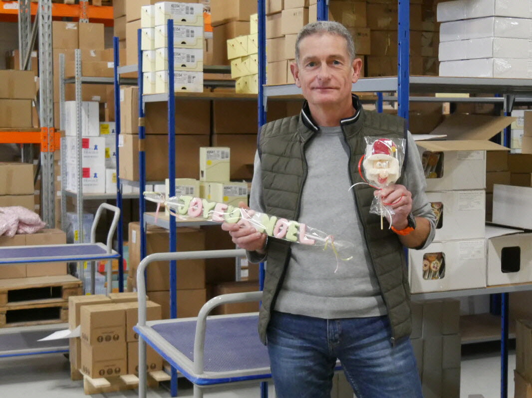 Homme présentant les produits de la marque Caramel Bonbon & Chocolat dans un entrepôt, mettant en avant la qualité et la diversité des confiseries artisanales destinées aux particuliers.