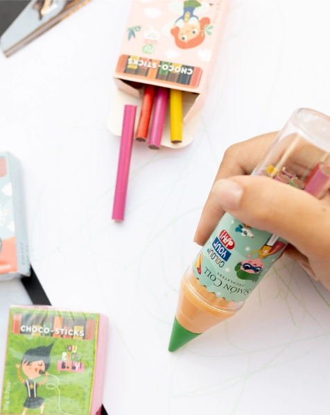 Maxi crayon vert en chocolat au lait écrivant sur une feuille, friandise originale mêlant créativité et gourmandise.